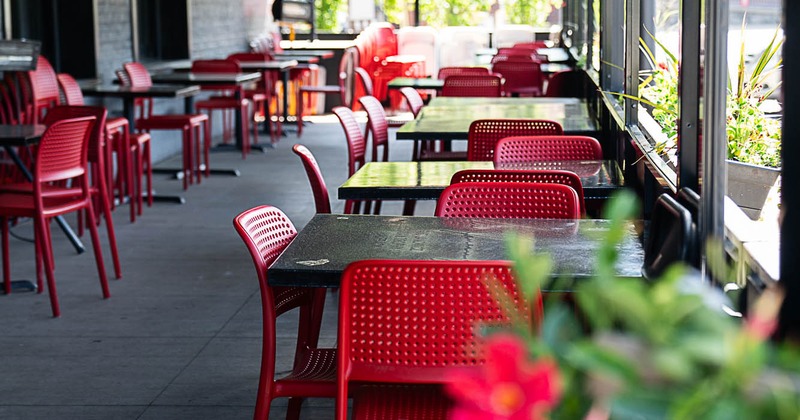 Interior, covered patio, tables with red chairs, ready for guests