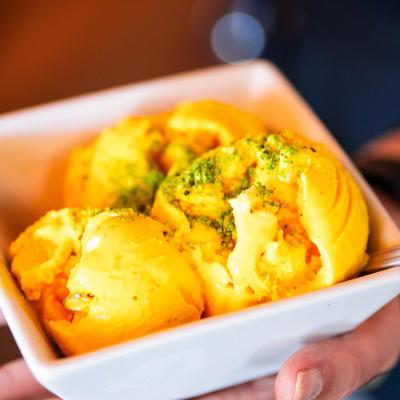 Three scoops of mango ice cream topped with finely chopped pistachios.