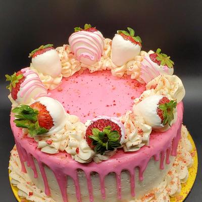 A round cake with pink icing drips and white chocolate-dipped strawberries on top.