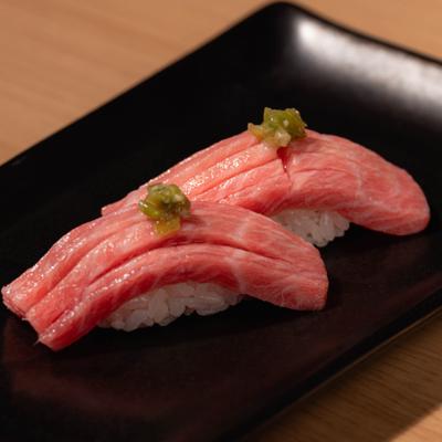 Bluefin tuna otoro nigiri with green topping on a black plate.