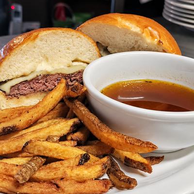 A halved beef sandwich served with fries and a bowl of dipping jus..