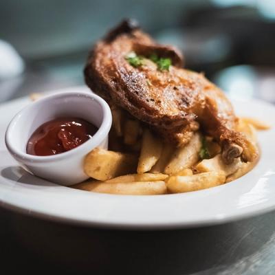 A plate of crispy fries topped with a grilled chicken piece, served with ketchup.