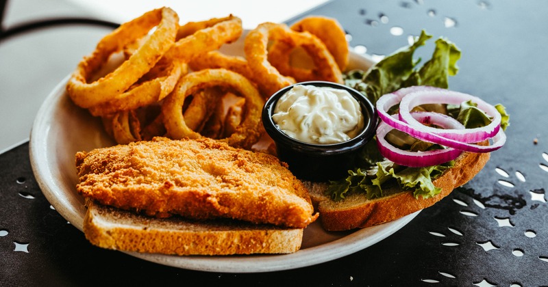 Fried white fish sandwich with onion rings and horseradish sauce on the side