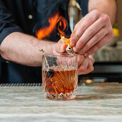 Bartender flames orange peel over a glass of Old Fashioned