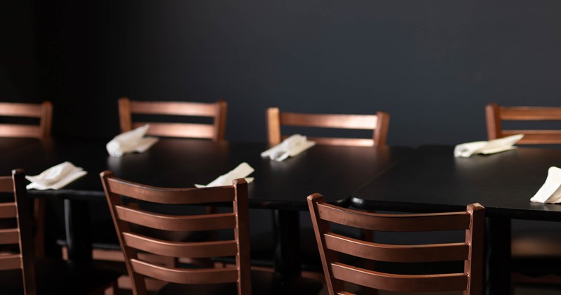 A dark wooden dining table with wooden chairs and neatly folded white napkins.
