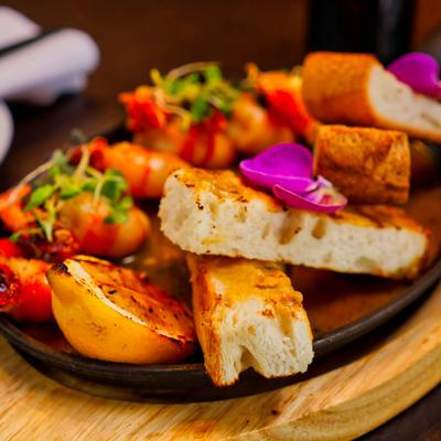 Butter-poached prawns with toasted bread and charred lemon, garnished with microgreens and flowers.