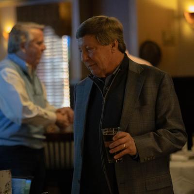 Men are in a restaurant holding beer, with tables and diners in the background.