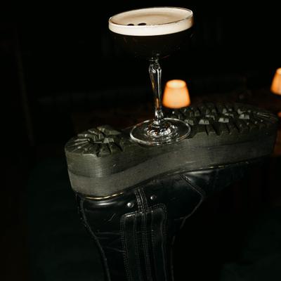 Espresso martini sits on the sole of a black boot.