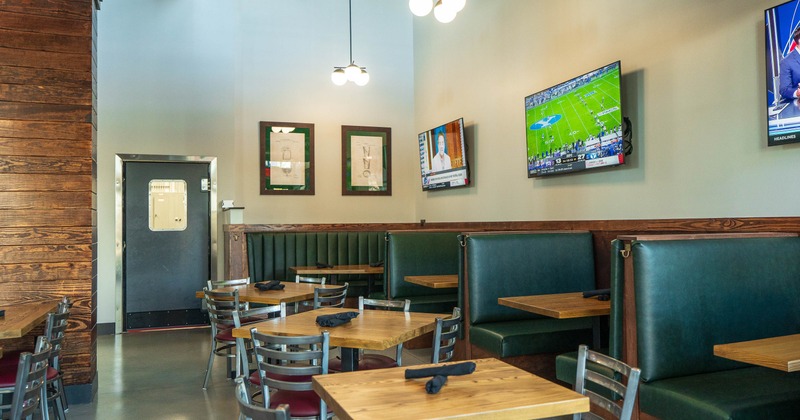 Restaurant interior with booth seating, wooden tables, and wall-mounted TVs.