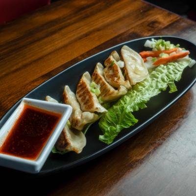 Fried dumplings plated with garnish and soy-based dipping sauce.