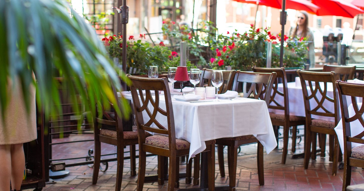 Outdoor patio dining at Il Sogno Italiano with white tablecloth tables, red umbrellas, and lush greenery.