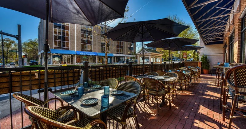 Outdoor patio dining area - tables, chairs and umbrellas along a brick path beside a building.