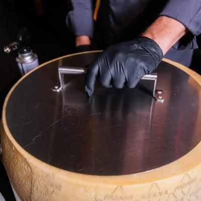 Chef lifting a lid on a cheese wheel.