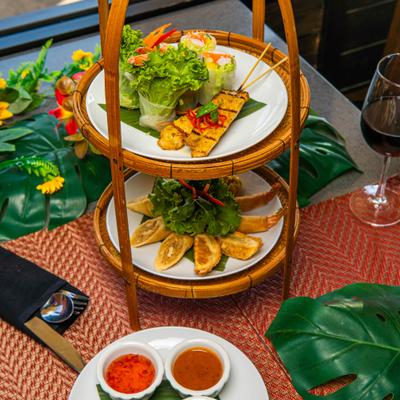 Bamboo tiered stand with fresh spring rolls, chicken satay, dumplings and sauces on the side.