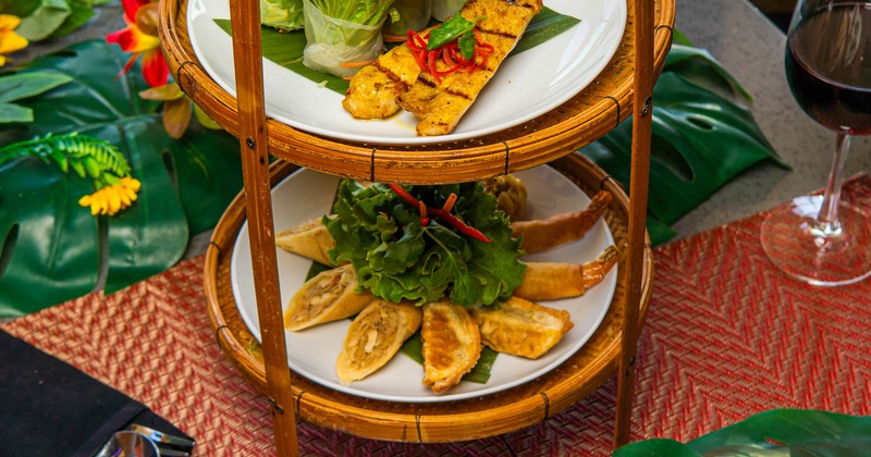 Appetizers arranged on a multi-tiered bamboo stand with sauces on the side