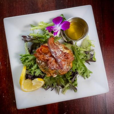 Crab cake appetizer topped with crispy bacon over a bed of mixed greens.