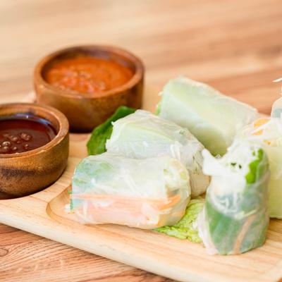 Veggie Rolls served on a wooden board with peanut sauce and sweet chili sauce.