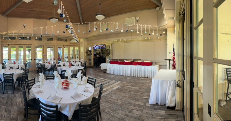 A decorated banquet hall with round tables, festive string lights, and a buffet setup