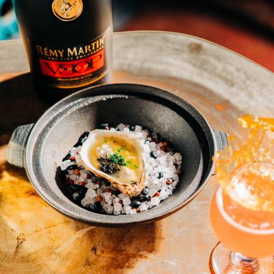 An oyster on salt beside a bottle of cognac and a cocktail.