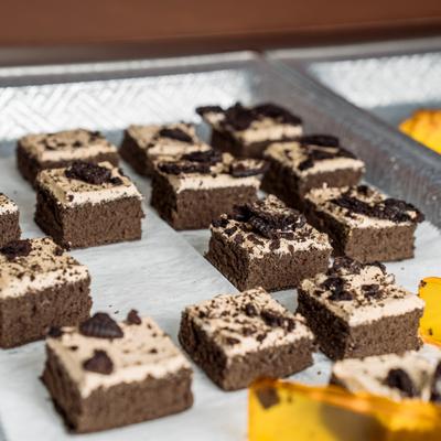 Small square chocolate cakes topped with frosting and crushed cookies on tray.