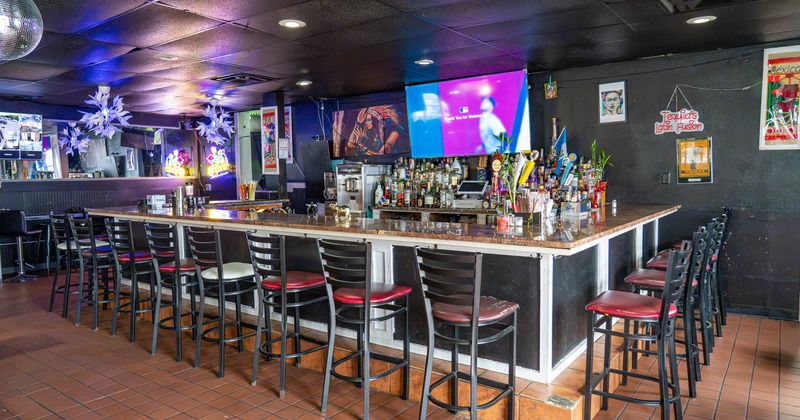 Bar area with high stools, colorful lighting, and multiple TVs