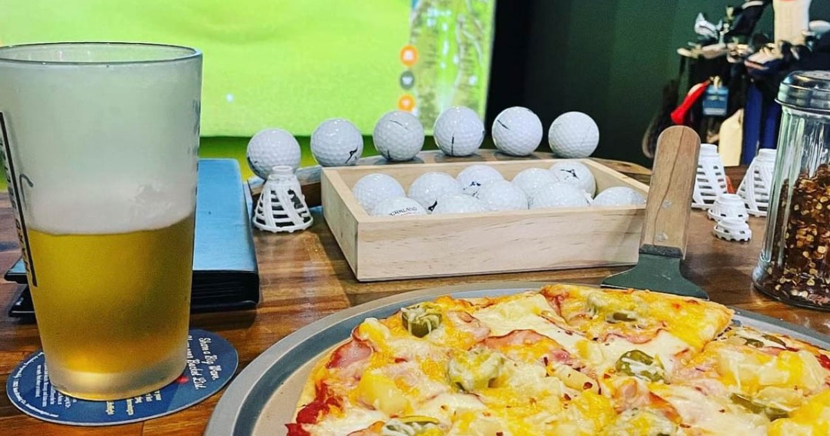 Pizza and beer on a table with golf balls and tees, simulator screen in the background