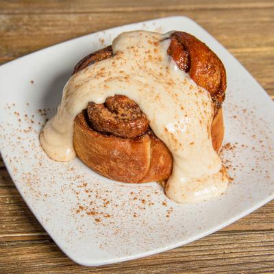 Cinnamon roll with icing on white plate, on a wooden table