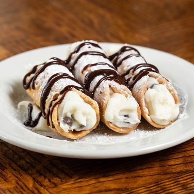 Three cannoli drizzled with chocolate on a white plate.