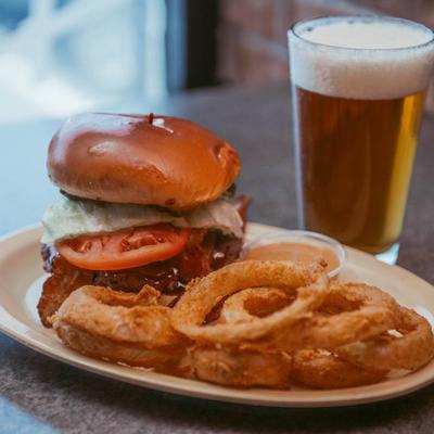 Bourbon burger with bacon, lettuce, and tomato, served with onion rings and a beer.
