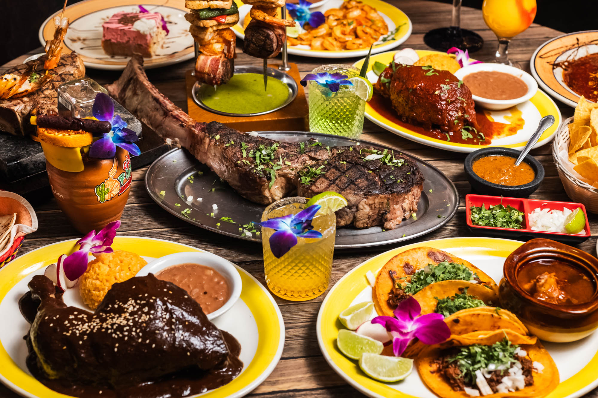 Grilled tomahawk steak surrounded by various dishes and cocktails