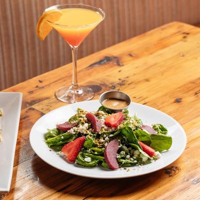 Strawberry and spinach salad with goat cheese and dressing served with a cocktail.