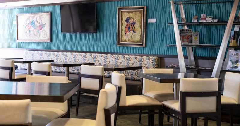 Interior - tables, cushioned chairs, a patterned bench, framed artworks, a flat-screen TV on a wall.