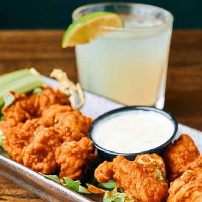 Boneless wings served alongside a white dipping sauce and a citrus cocktail.
