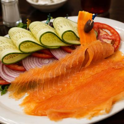 Thinly sliced smoked salmon served on a white plate with fresh vegetables.