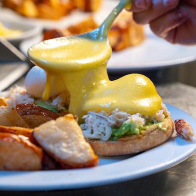 Hollandaise sauce being poured over a crab and avocado sandwich.