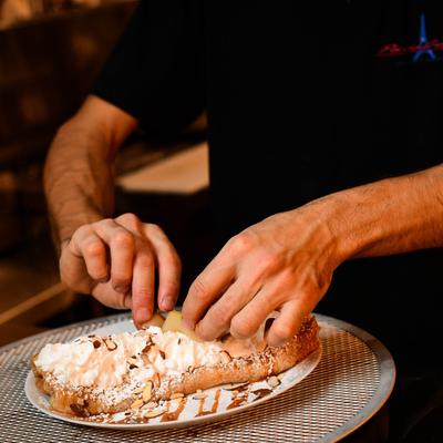 A person garnishing a Pear Caramel Crepe.