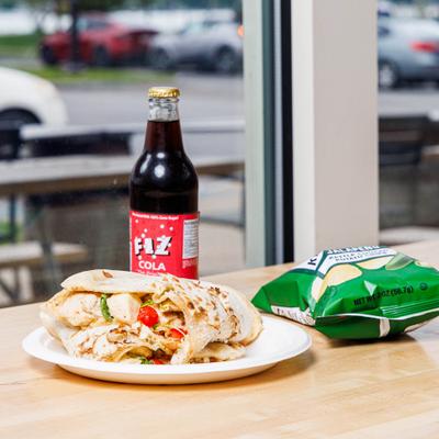 Otisco Panuozzi served on a wooden counter with a bag of chips and a drink.