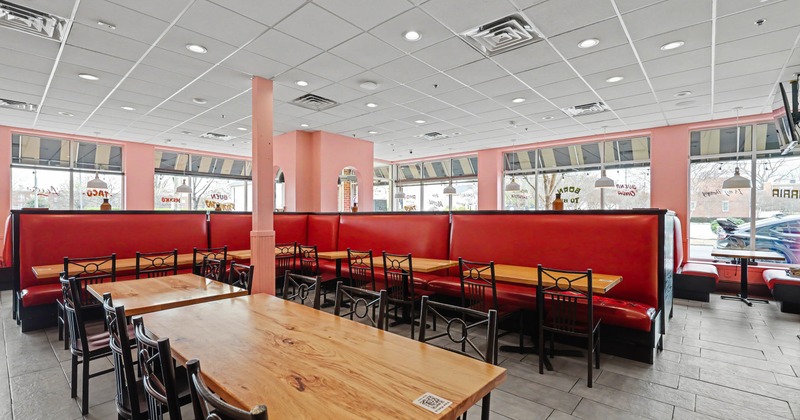 Interior of a restaurant with red booths, wooden tables, metal chairs, pink walls, and large windows