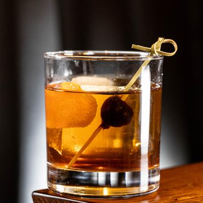 Old Fashioned cocktail with orange peel and cherry garnish.
