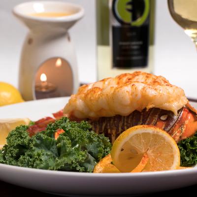 Lobster dinner with kale and lemon slices, candle and wine in the background.