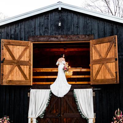 A person to be wed standing on a barn balcony with their wedding dress trailing.