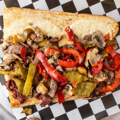 Steak sandwich with peppers and mushrooms on checkered paper.