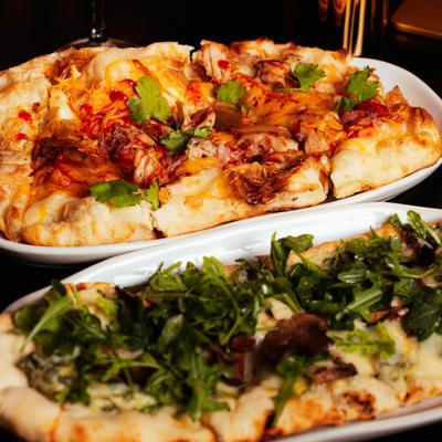BBQ chicken flatbread and mushroom arugula flatbread on white serving platters.