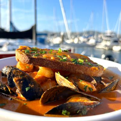 Seafood stew with mussels and toast against a sunny marina background.