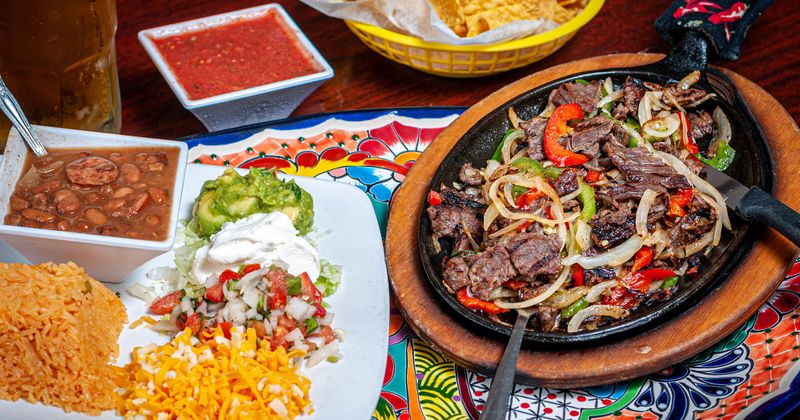 Beef Fajitas plate, salsa, and a plate with beans, rice, pico, sour cream and guacamole