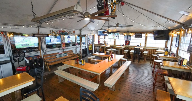 Interior, dining area with wooden tables, benches, and several TVs, sports memorabilia