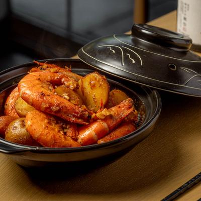 Braised shrimp served in a traditional black ceramic pot with potatoes and garlic.