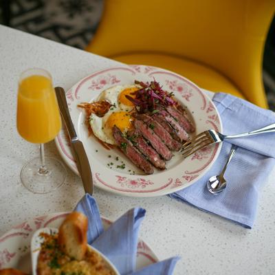 Steak and eggs served with a glass of orange beverage.