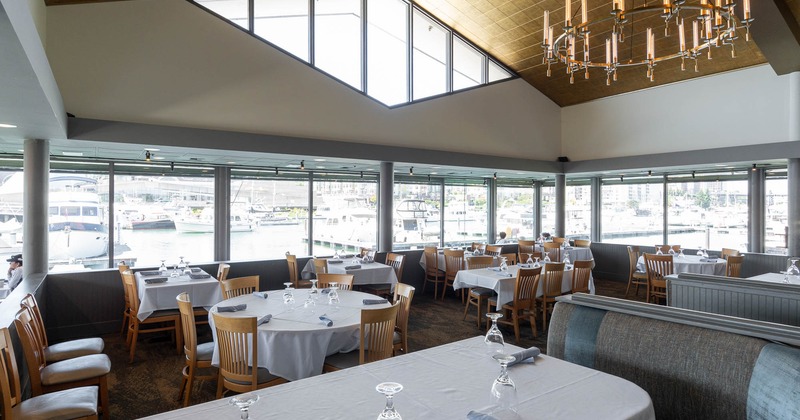 Restaurant interior with tables set near large windows overlooking a marina