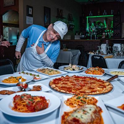 Chef standing proudly by a table with assorted food dishes on it.
